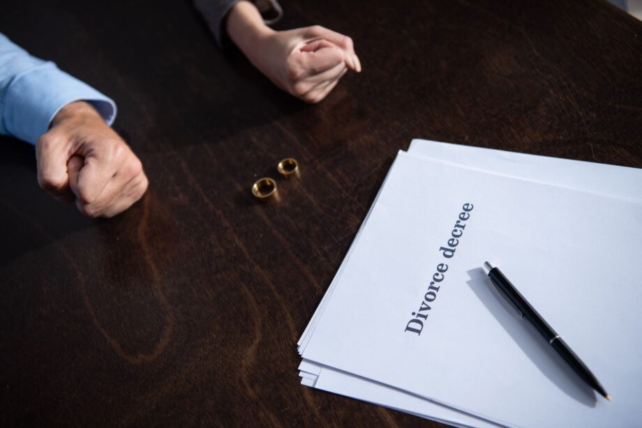 Two spouses sitting across from each other with wedding rings and divorce decree document on table representing Dallas divorce proceedings