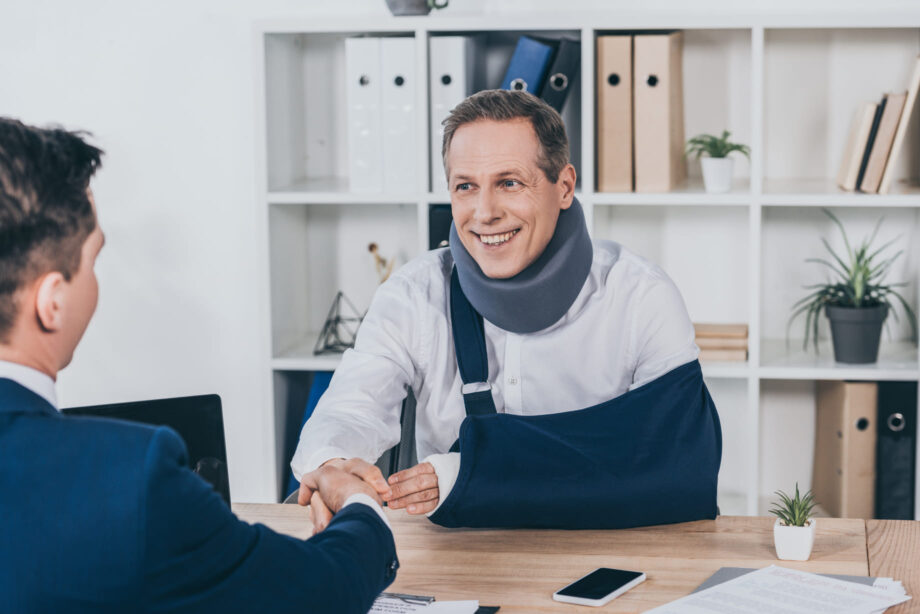 Injured client wearing neck brace and arm sling shaking hands with Dallas personal injury attorney after successful consultation