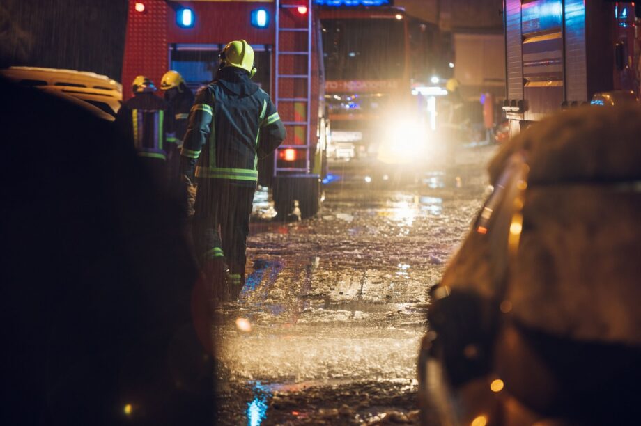 Firefighters and emergency responders working a serious truck accident scene on a rain-soaked Dallas road at night with emergency lights flashing