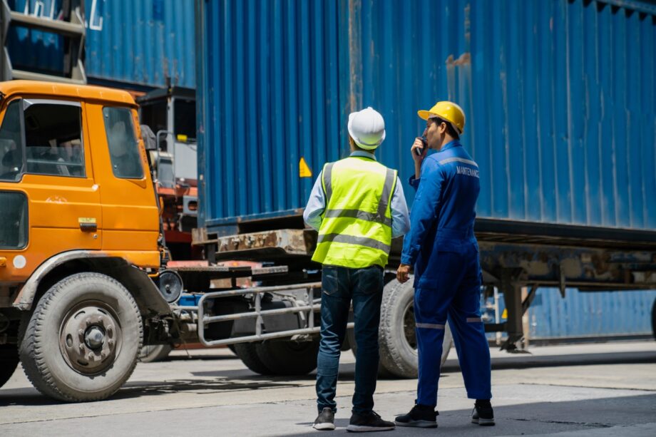 Two maintenance workers in safety gear inspecting a commercial freight truck representing FMCSA vehicle inspection and federal trucking regulation compliance requirements