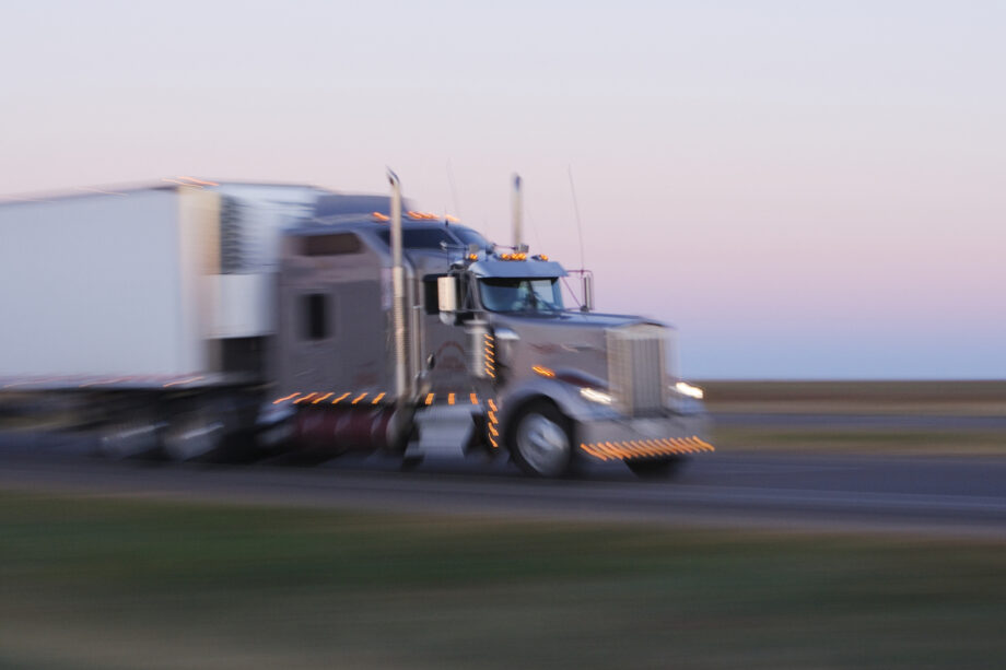 Motion blur of a commercial semi-truck with amber running lights driving on a Texas highway at dusk representing state and federal trucking regulations